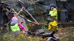 En flicka och en pojke från dagisgruppen Valhajarna bygger en koja av kvistar och träbitar vid en klippa på Drumsö.