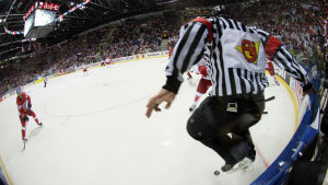 Arkivbild. En ishockeydomare hoppar för att akta sig för pucken.