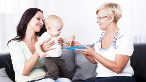 Många av er skriver att svärmors hjälp och stöd är ovärderlig. en ung kvinna sitter i en soffa, har ett litet barn i famnen, en äldre dam sitter bredvid henne och ger en leksak till barnet.