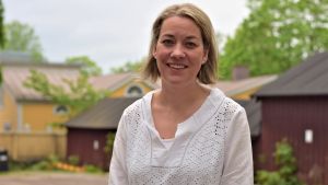 Ekenäs gymnasiums rektor Petra Blomqvist. Kvinna i vit skjorta utomhus ler mot kameran. I bakgrunden träd och trähus.