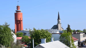 Från vattentornet i Hangö kan man se långt, men däremot inte sia hur den politiska framtiden i staden ser ut. Hangö vattentorn och kyrka fotograferat från bro. Man ser hustak, gröna träd och knallblå sommarhimmel