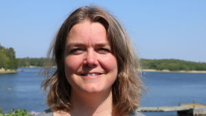 Anette Norrgrann. En kvinna med axellångt mörkt hår. I bakgrunden syns hav och skog.