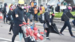 Militanta demonstranter förbereder sig för att drabba samman med kravallpoliser. Brandsläckarna används som vapen. Man iklädd hjälm och andningsmask skjuter kärra innehållande brandsläckare framför sig.