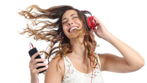 Om du dansar och sjunger med blir lyckoeffekten ännu större. En kvinna med långt lockigt hår lyssnar på musik i hörlurar, från sin smarttelefon. Hon ser väldigt glad ut. Hon ler och dansar.