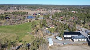 En drönarbild visar hur det ser ut kring en fastighet. En flygbild över en golfbana, åkrar och hus då våren börjar grönska i träden.