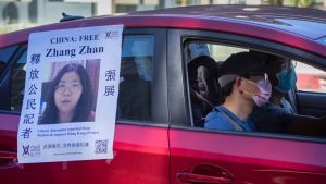 Journalisten Zhang Zhan som varit fängslad för sin coronarapportering sedan maj har fått mycket stöd både i Kina och utomlands. Nu har hon dömts till fyra års fängelse. Två personer i munskydd sitter i en röd bil. På bilen hänger en lapp med en bild på journalisten Zhang Zhan och en uppmanan att fria henne från fängelset.