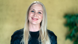 Zaida Bergroth är stolt över att det talas svenska i filmen. Zaida Berghroth ler och tittar in i kameran. I bakgrunden en gul vägg och en grön växt.