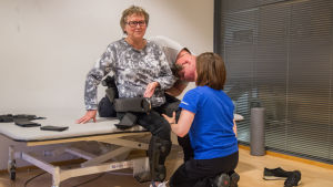 Maj-Len kläs på exoskelettet. Daniel Söderman och Katri Pihlaja-Kuhna klär på Maj-Len Sjöberg ett exoskelett