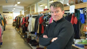 Juha Palin i Ekokaarinas loppislokal. Medelålders man med svart tröja står framför en hylla med loppisgrejer.