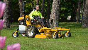 Trädgårdsarbete är ett vanligt sommarjobb för unga. En ung man sitter på en gräsklippare och klipper gräs i en park.