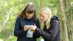 Jenny Salmi och Camilla Norrgård tittar på mottagaren. Två tjejer håller i en mottagare i en skog.