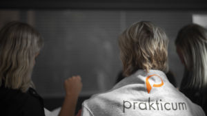 Prakticum är inte med i Helsingfors pilot med gratis läromaterial. En kvinna står och pratar med en annan kvinna. På den ena kvinnans rygg står det "Prakticum. En skola - många möjligheter."