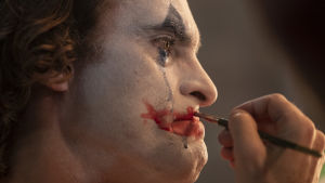 Arthur på väg att bli Joker. Närbild då Arthur (Joaquin Phoenix) sminkar sig till clown samtidigt som han gråter och blå mascara rinner nerför kinden.
