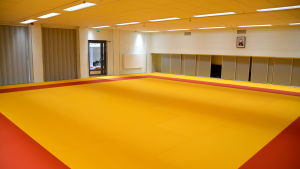 Ett av rummen under studentbostäderna på Borgmästargatan. Här tränar bland annat Porvoo Aikikai. En tom sal med gul-röd tatami matta.
