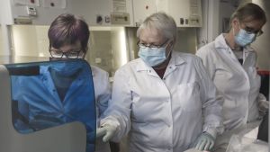 Tre kvinnor undersöker coronavirusprover i laboratoriemiljö.
