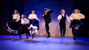 En scen på ÅST från 1914 på ön Hustrun. På bilden en scen på Åbo Svenska Teater som ska utspela sig år1914 på ön Hustrun. Ett gäng unga dansar och hoppar.