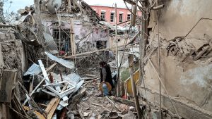 En kvinna vandrar bland ruiner efter bombardemang av Ganja i Nagorno-Karabach 6.10.2020 Nainen kulkee raunioiden keskellä raskaiden kantamusten kanssa.