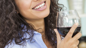 Många kvinnor undviker hormonbehandling av rädsla för cancer men två glas vin per dag utgör en större risk än hormonerna, leende kvinna med rödvinsglas