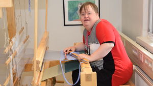 Misu Engblom har designat bland annat bilderna på penaler och väskor. Misu Engblom sitter vid en vävstol.