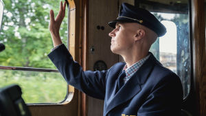 Tavallisesti Kimmo Kuosmanen ajaa moderneja, automaattivaihteilla varustettuja junia työnantajansa VR:n piikkiin. Junankuljettaja univormussaan heilauttamassa kättään junan ikkunassa.