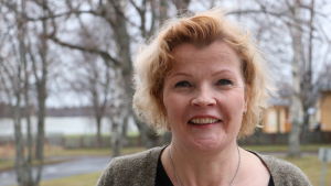 Minna Nikander välkomnar fler invånare till staden. En kvinna i 50-årsåldern med axellångt rödbrunthår ler. I bakgrunden syns träd.