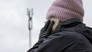 I stället för att åka hem till klienten, kan hemvårdaren i vissa fall ringa för att kolla att allt är bra. Kvinna utomhus, talar i mobiltelefon. I bakgrunden skönjer man en mobilmast.