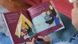 I dag finns det barnböcker som bryter gamla könsroller. Flickor ses i rollen som superhjältar och pojkar leker med Barbiedockor. En person läser boken Ihmeellinen Minna ja suomalaiset supernaiset av Elina Lappalainen.