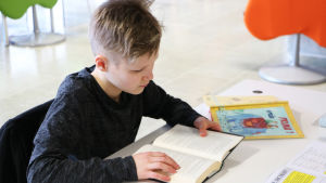 En pojke sitter och läser i en bok.
