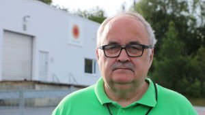 Håkan Blomqvist. En man med grått hår, mustasch och glasögon står på en fabriksgård.