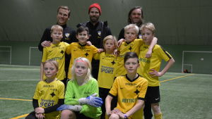 Åbo IFK P11. Översta raden från vänster: Kim Friman - Markus Lauri - Peter Nuyttens. Från vänster andra raden: Otava Uskelin - Oliver Österlund - Totti Forsman - Harald Lundqvist - Michel Pettersson. Nedersta raden från vänster: Hugo Oksjoki - Dan Lauri - Alvin Udd Pojkar 11-laget från ÅIFK står tillsammans med sina tränare på en konstgjord gräsplan inomhus.
