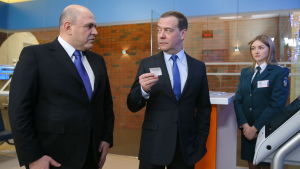 Michail Misjustin med den före detta premiärministern Dmitrij Medvedev. Två kostymklädda män tittar på varandra. Den ena håller upp en lapp. I bakgrunden står en kvinna i uniform som tittar åt sidan.