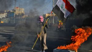 Också i Najaf, cirka 160 kilometer söder om Bagdad, brann bildäcken på måndagen. En demonstrant i Najaf, cirka 160 kilometer söder om Bagdad, bar på Iraks flagga bland brinnande bildäck på måndagen.