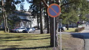 Vid Ystadsgården finns i dag några parkeringsplatser. I förgrunden en parkeringsförbudsskylt, i bakgrunden bilar och ett vitt gammalt trähus.