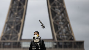 Hengityssuojaan pukeutunut nainen seisoo Eiffel-tornin edessä.