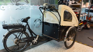 En elcykel på tre hjul har många användningsområden och blir allt mer populär bland kunderna, menar försäljaren Mika Sevón. Svart elcykel med tre hjul och en vagn framtill.