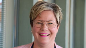 Kita Westerlund. En leende kvinna med kort ljust hår och glasögon står intill ett fönster.