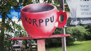 Punaisessa, kahvipannun muotoisessa kyltissä teksti "Korppu". 