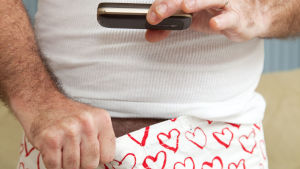 En bild av en man som fotar ner i sina boxershorts, med en mobiltelefon.