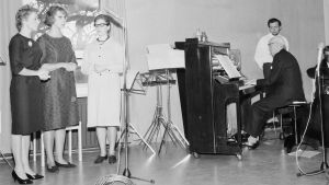 Sigurd Snåre spelar piano medan Majlen Sandström, Majlis Ede och Marita Lax sjunger. Här invigs Radio Västnylands renoverade studio 18.10.1964. Radion startade sin verksamhet i samma hus år 1947, men fick renoverade lokaler först flera år senare. En man spelar på piano och tre kvinnor sjunger.