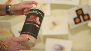 Den här tomma plastflaskan har hängt med i över 50 år. Fortfarande sitter färgerna kvar. Frågan är vad som är värre, det forna innehållet eller giftet i färgerna... En mycket gammal, lite söndrig plastflaska är man haft hushållssprit. Ungår i en utställning med plastskräp som plockats upp på stränder i Hangö.