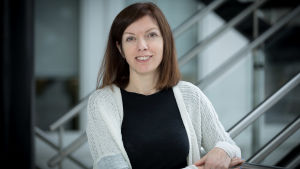 Forskningschef Eleanor Coffey leder forskarteamet som deltar från Turku Bioscience. Eleanor Coffey, en brunhårig kvinna med vit kofta och svart t-skjorta står i en trappa