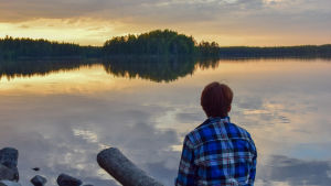 "Kansallispuistoihin mennään nauttimaan hienoista maisemista ja saamaan luontokokemuksia", sanoo tutkimusprofessori Liisa Tyrväinen Luonnonvarakeskukselta. Ihminen istuu auringonlaskussa järven rannalla