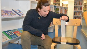 Benjamin Lundin visar en stol som har snittats sönder. Benjamin Lundin visar en trasig stol i Ingå bibliotek.