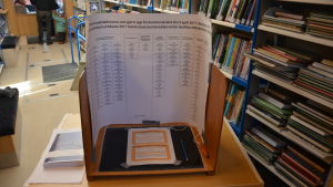 Kandidaterna i Raseborg syns på skärmen i valbåset men väljare skrivna i andra delar av landet hittar information om sina kandidater i boken till vänster på bilden. Valbås i valbussen i Raseborg.