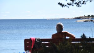 Plagens badstrand i Hangö har många besökare under soliga dagar. En bild på en person som sitter på en bänk och tittar ut över havet.