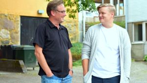 Stefan Haglund och Gustav Lundström bryr sig inte nämnvärt om någon ropar hurri ät dem. En man i mörk t-skjorta och med glasögon och en yngre man i vit t-skjorta och grå kofta. I bakgrunden en gul stenbyggnad och ett träd.