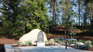 Det är inte mycket som skiljer skogen där askan sprids från en vanlig skogsdunge, men den stora stenen och minnesplattan med bibelcitat avslöjar platsens andliga art. Minnesplatta med bibelcitat framför en stor natursten.