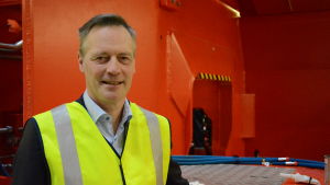 Mats Eriksson. En man står framför en stor röd lastare. Mannen har på sig en grön skyddsväst.