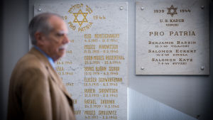 Namn på judar som stupat i kriget hänger på väggen i synagogan i Helsingfors. Tietokirjailija ja tiedottaja John Simon, Helsingin juutalainen seurakunta, Pro Patria -taulun edessä, 3.10.2017.