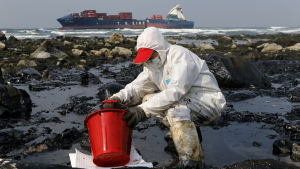 Oljesaneringsarbete efter tankfartygsolycka i Taiwan 2016. Man i skyddsutrustning som försöker putsa olja bort från stranden i Taiwan.